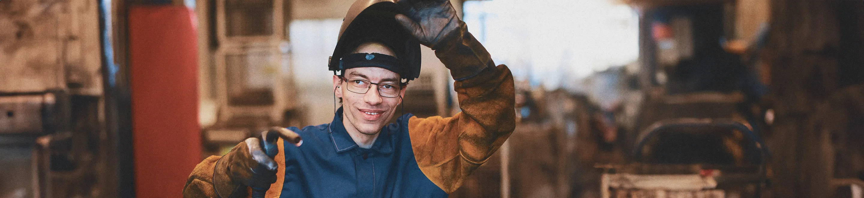 Ein junger Mann mit einem Schweißerhelm in einer Werkstatt.